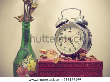 Still life with broken alarm clock, old glass vase with dead rose, perfume, vintage box, toned image.