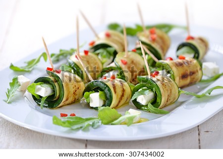 Delicious rolls of fried zucchini slices and feta cheese with rucola, served with olive oil and pieces of bell peppers