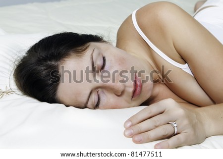The beautiful young woman sleeps on white bed lying on one side