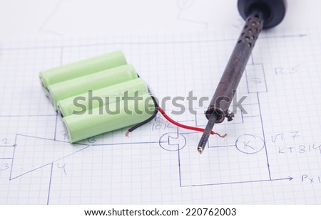 A soldering iron and battery on a background of the electric scheme