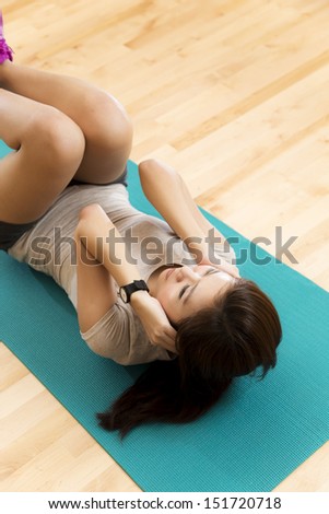 Vertical shot of an Asian lady doing her sit ups exercise in a gym.
