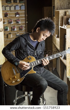 A vertical shot of a young asian man playing electric guitar.