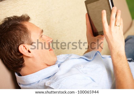 Man relaxing with tablet, laying on sofa in home with big window in background, close up