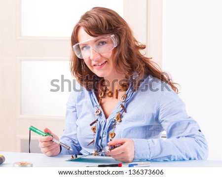 Beautiful woman in protective glasses fixing computer parts with soldering iron and other tools