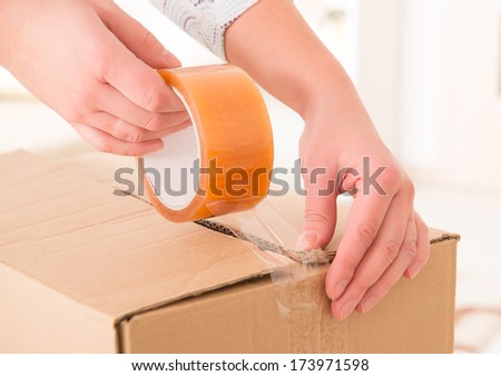 Hands with roll of transparent packaging, adhesive tape on a cardbox