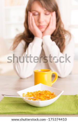 Sleepy young woman trying to eat cornflakes and drink morning coffee