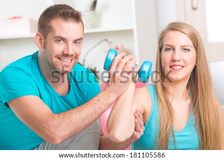 Beautiful young woman doing exercises with dumbbells with personal trainer at home