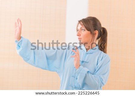 Beautiful woman doing qi gong tai chi exercise wearing professional, original Chinese clothes at gym