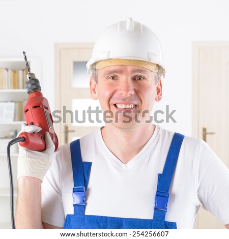 Smiling man with electric drill wearing protective helmet