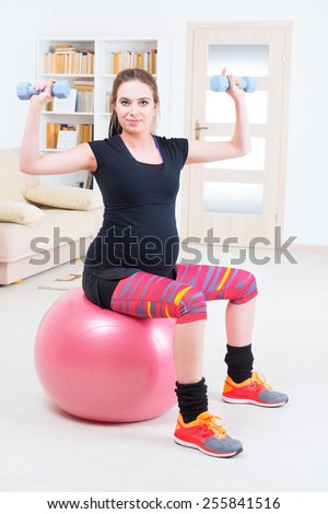 Young pregnant woman exercising with dumbbells and gym ball at home