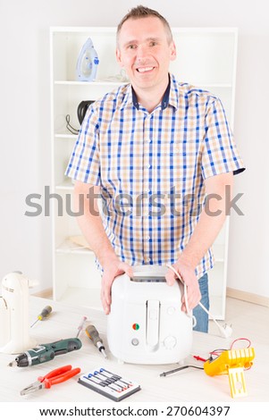 Smiling man holding repaired deep fryer at home appliance service workshop