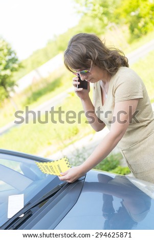 Suprised woman looking on parking ticket placed under windshield wiper and talking on the mobile phone