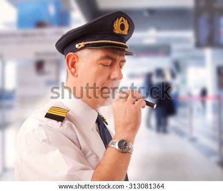 Airline pilot wearing uniform with epaulettes smoking electronic cigarette.