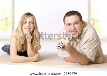 Young woman and man lying on the floor in the room. Man is holding a remote controller.