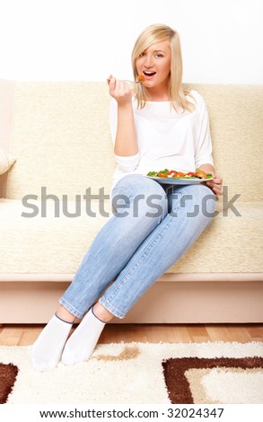 Beautiful woman sitting on the sofa and eating a healthy vegetable greek salad.