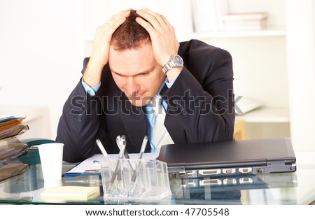 Stressed businessman sitting at desk holding his head and worrying
