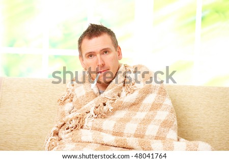Man with cold sitting on sofa with thermometer in mouth