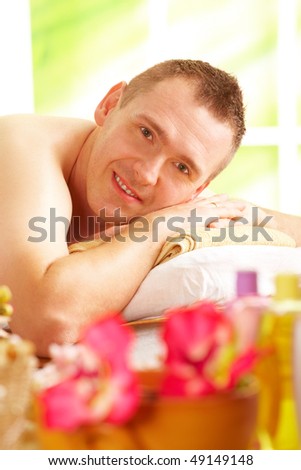Man resting in sunny spa salon laying on the mat with flowers and cosmetics in foreground