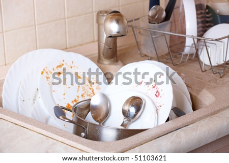 Pile of dirty dishes like plates, pot and cutlery in the light beige granite sink
