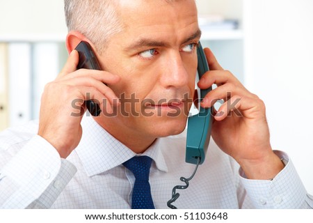 Mature businessman with two phones, in the hurry in his office.