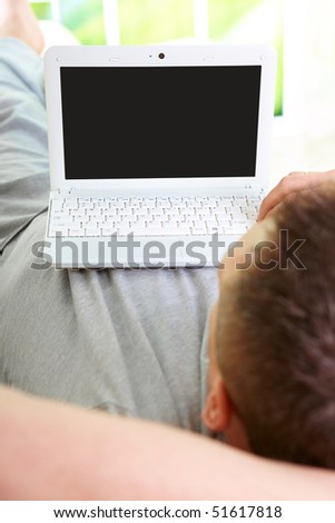 Man relaxing on sofa with laptop. View from above his shoulder to expose nice LCD display.