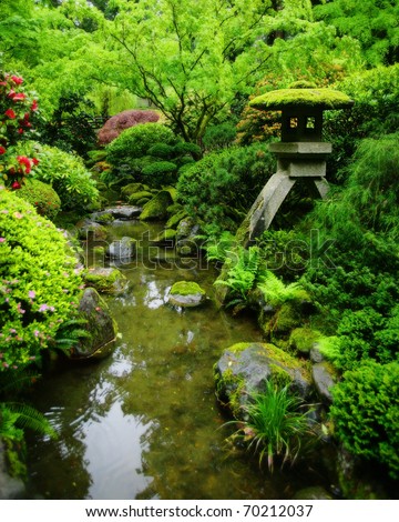 A lush green Japanese garden with Japanese lantern, and moss covered rocks.