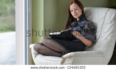 young woman sits on chair  and reading book