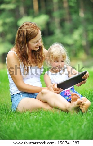young mother with her daughter  looking at screen of laptop. summer day.