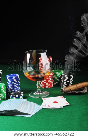 Cigar, chips for gambling, drink and playing cards on green