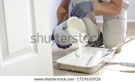 Man pours paint into the tray and dips roller. Professional interior construction worker pouring white color paint to tray. Stock fotó © 