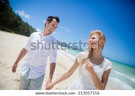 Couple in white clothes walking on a deserted tropical beach with bright clear blue sky