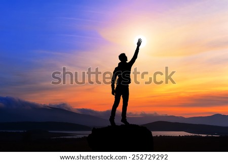 happy man with hand up on sunset background, man on top of the mountain reaches for the sun, silhouette man holding sun on the hill