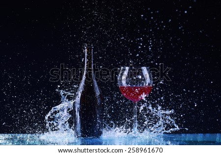 bottle and glass with red wine, water splash, wine on table on dark black background, big splash around Glass and bottle of red wine splash on black