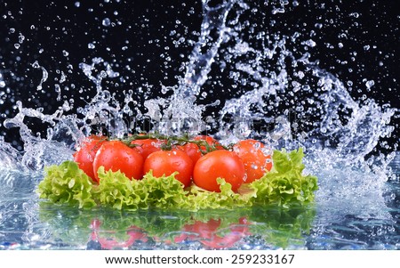 Fresh tomato cherry and green fresh salad with water drop splash on dark background Macro drops of water fall on the red cherry tomatoes and make splash