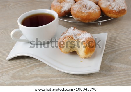 A cup of coffee and donut bitten in the powdered sugar on a plate