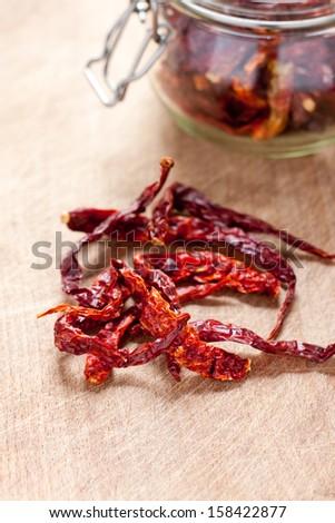 A group of dried red chillies in front of a jar