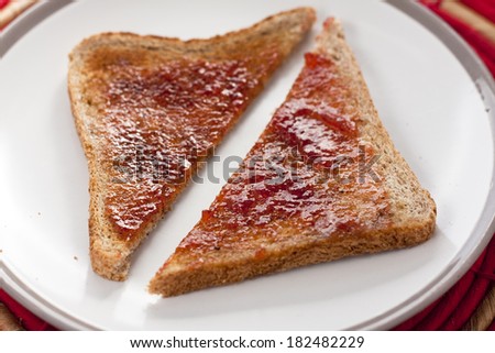 A slice of brown toast with strawberry jam cut diagonally