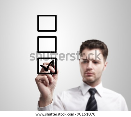 Young business man drawing a tick on a glass window in an office. Man choosing one of three options. On a gray background