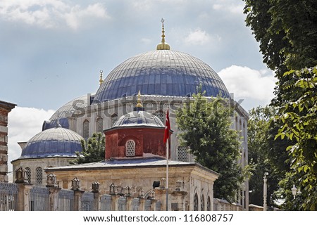 Shot taken outside the main gate to Hagia Sophia a monumental landmark in Istanbul over the queues of public waiting to tour of the historic building, blue cloudy sky and Turkish flag in the breeze