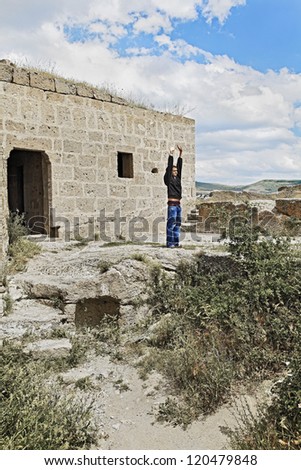 Trendy teenager outside a derelict religious building worshiping the sun. The shot location is a centuries old church now vacant and in ruins in a remote isolated part of Cappadocia in Turkey