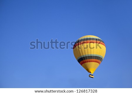 Aerial shot of yellow hot air balloon with colored bands in a clear blue sky. Generic image, shot location, Cappadocia, Anatolia, Turkey