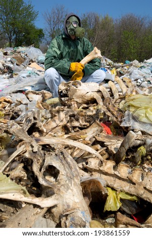 Man in a gas mask sitting on the garbage and holding a bone in his hand