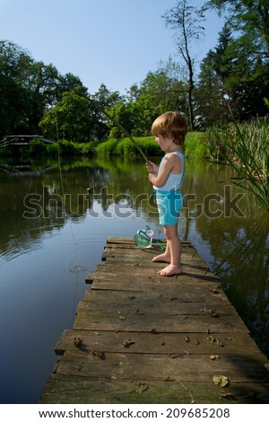 Sweet Little Boy Standing on the Edge of Wooden Dock and Fishing on  Lake in Sunny Summer Day