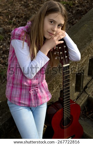 Three Quarter Length Shot of Young Girl Casually Dressed Leaning on Guitar and Looking at the Camera