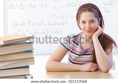 Highschool student sitting in classroom front of whiteboard, smiling.