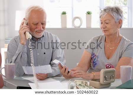 Elderly couple checking bills at home, discussing finances.