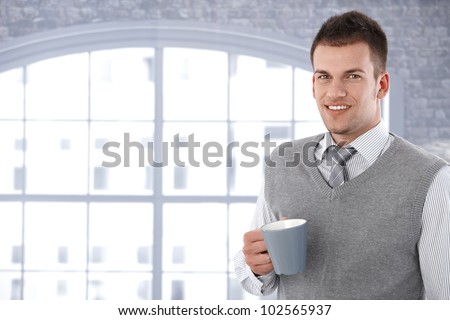 Portrait of young man drinking tea, smiling at camera.