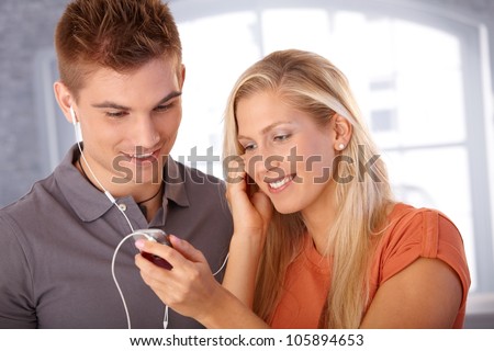 Smiling young couple listening to music together, sharing earphones.