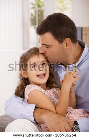 Father hugging and kissing little daughter, smiling.