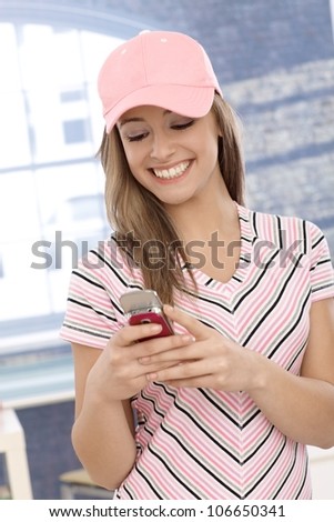 Casual girl in pink baseball cap using cellphone, smiling.